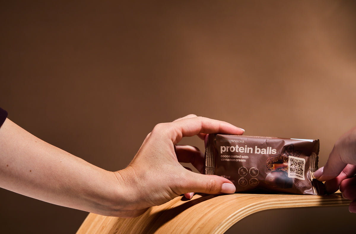 A hand holding a Cocoa Coated Protein Balls Cinnamon Cream packet