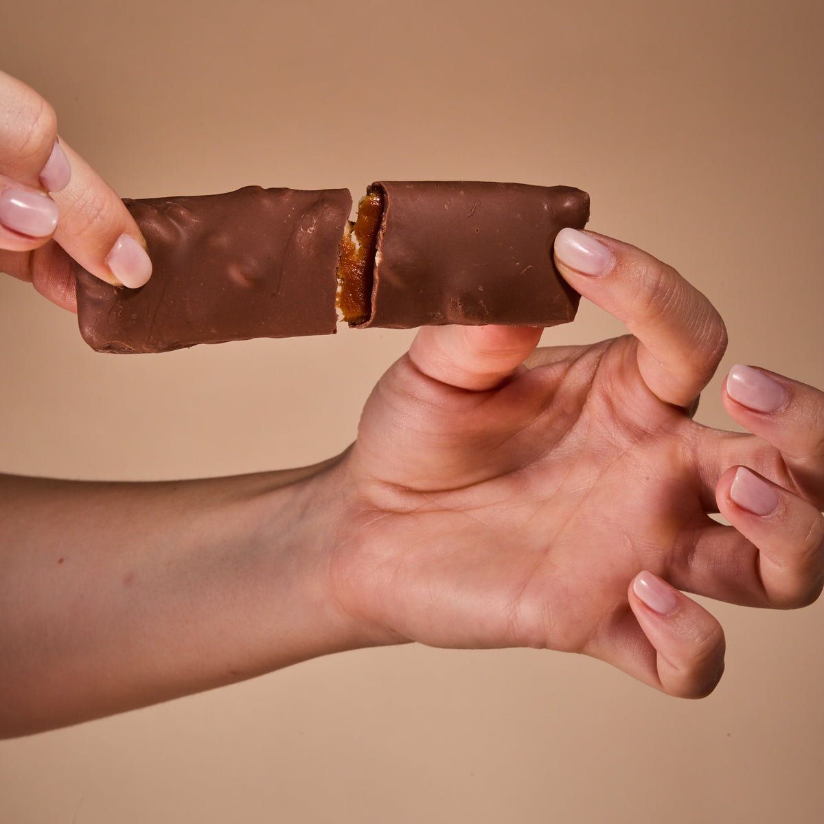 Hands breaking Protein Milk Chocolate with Salted Caramel in half